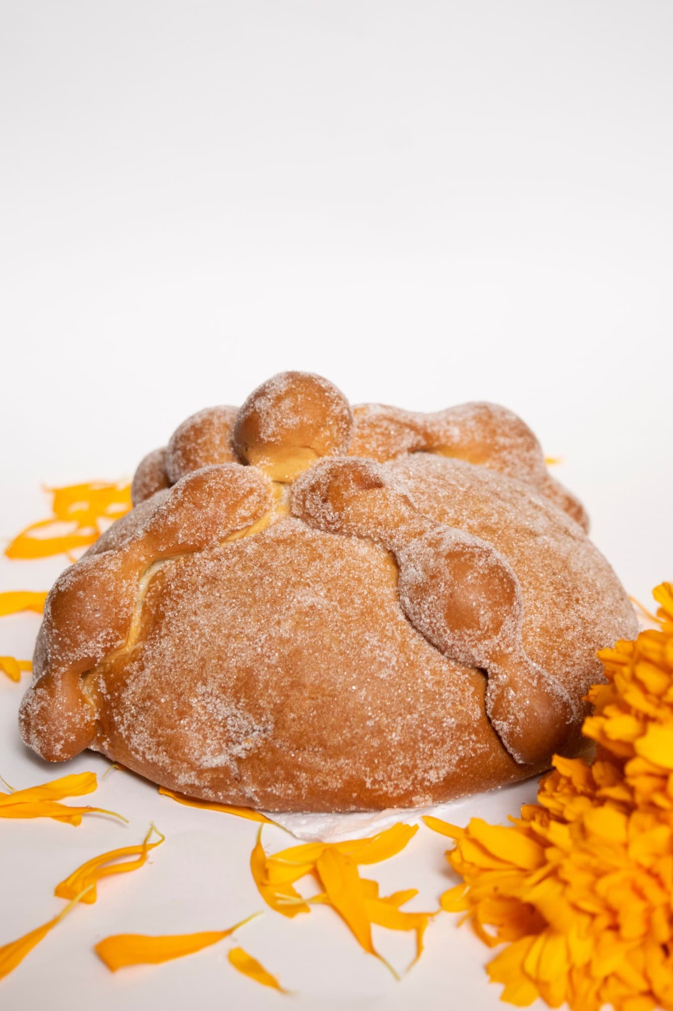 Pan de muerto espolvoreado con azúcar junto a flores de cempasúchil