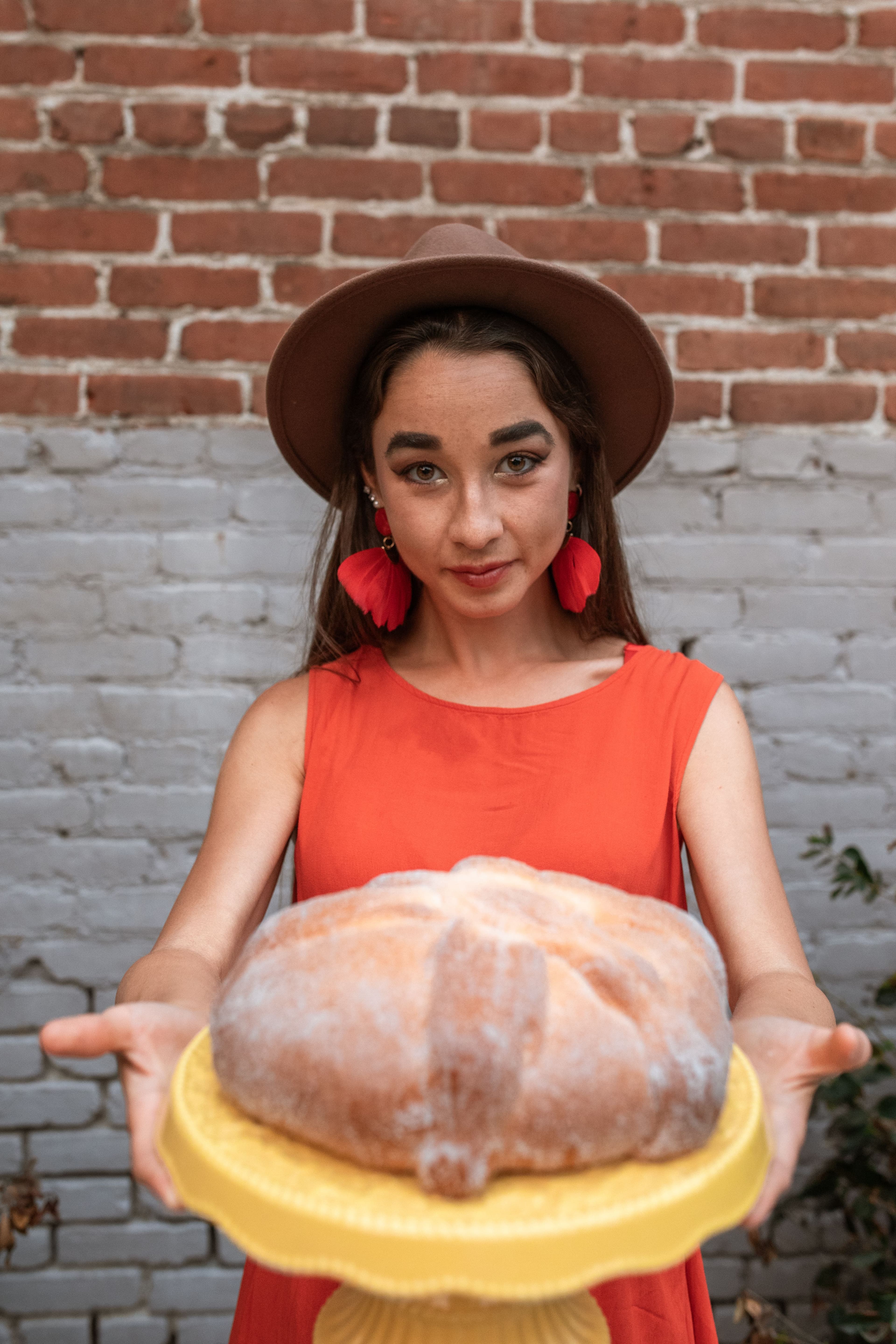 Mujer ofreciendo un pan de muerto grande sobre una base amarilla