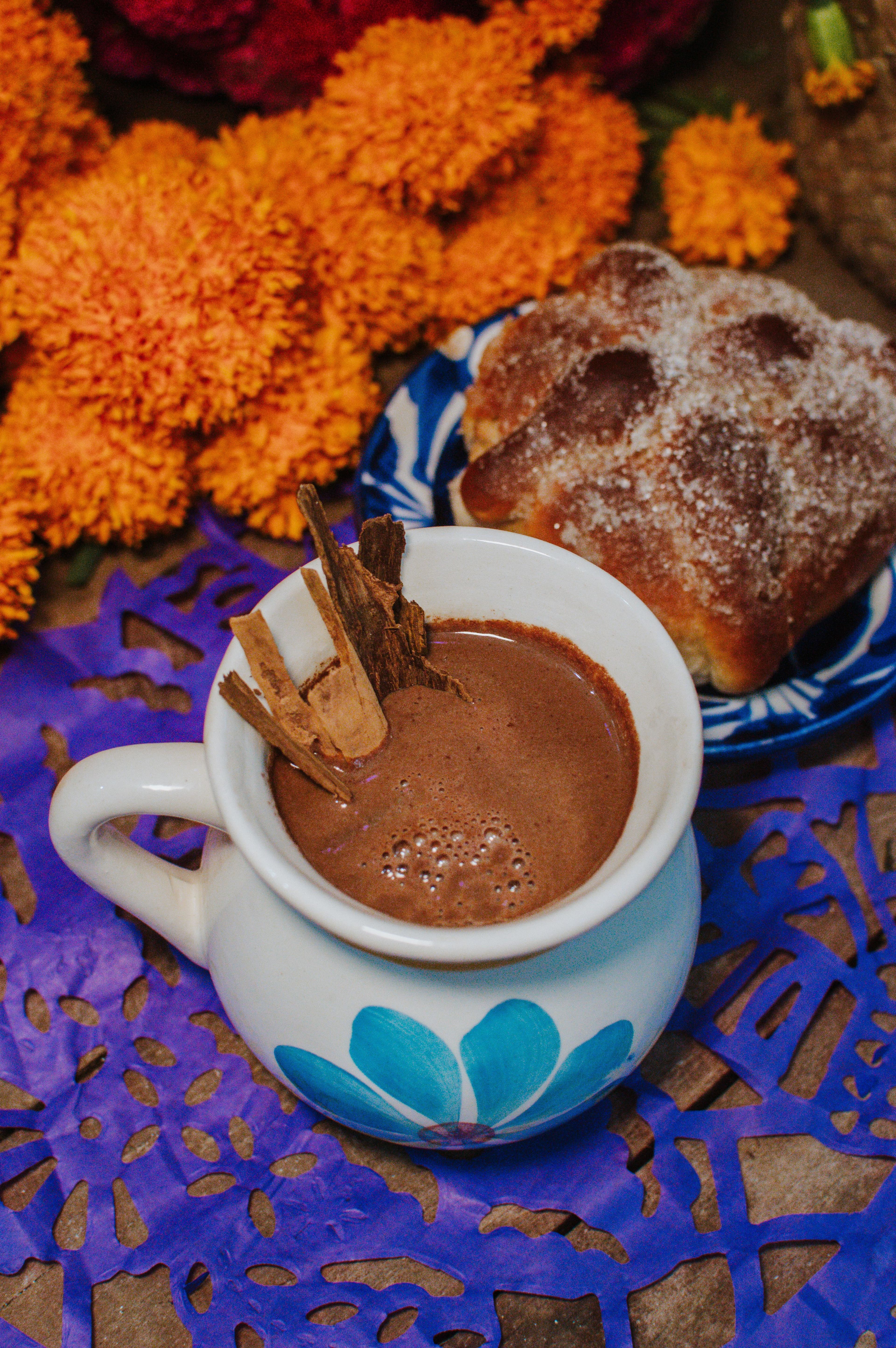 Pan de muerto y chocolate en jarrito sobre papel picado morado